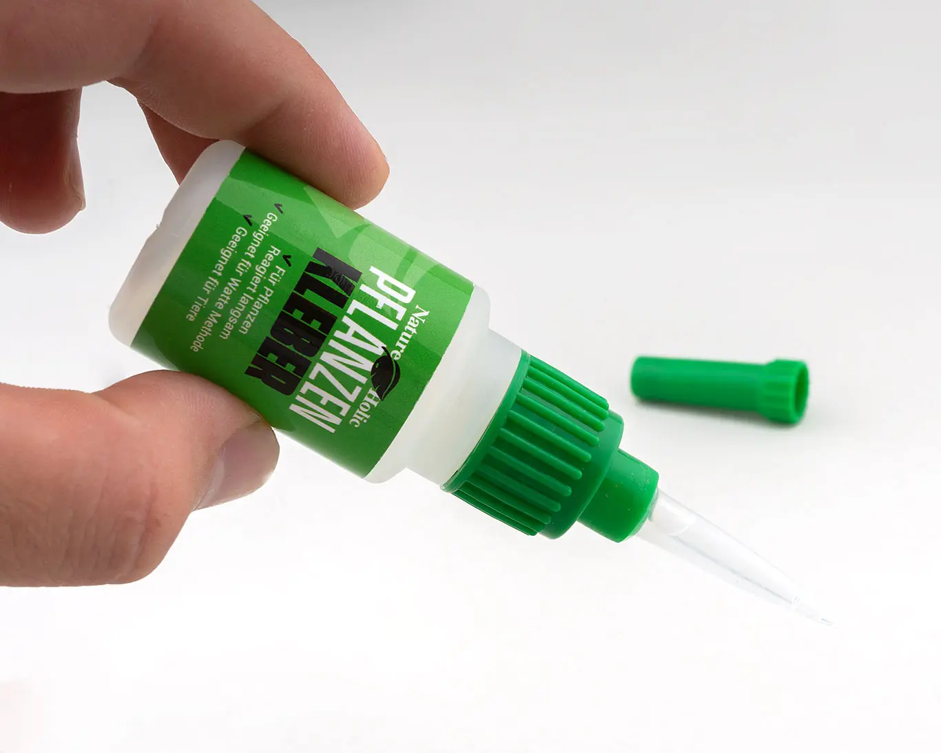 Hand hält Pflanzenkleber-Flasche mit grünem Verschluss